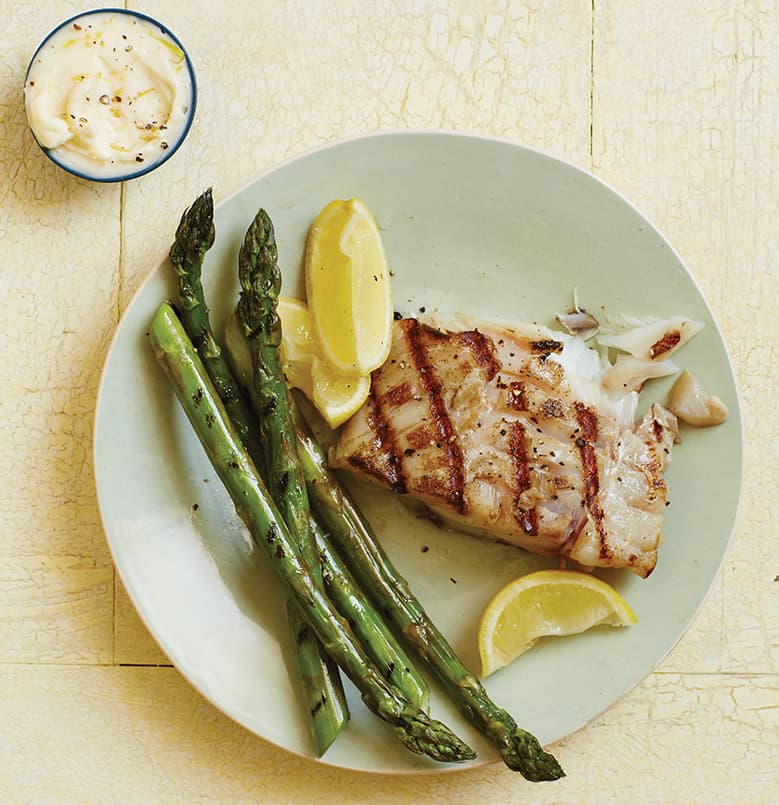 Pescado a la parrilla con limón y mantequilla sobre espárragos asados